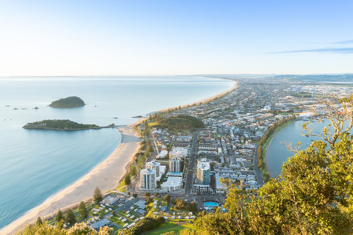 Mount Maunganui stretches out below as sun rises on horizon and falls across ocean beach and buildings stock photo